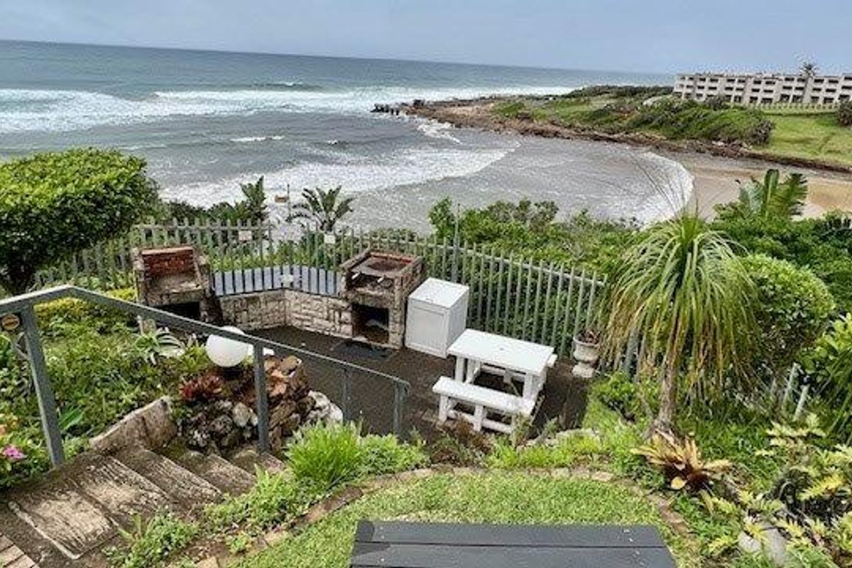 Rear outdoor area featuring a built-in brick braai, concrete stairs with metal handrails, and direct views of the coastline and ocean.