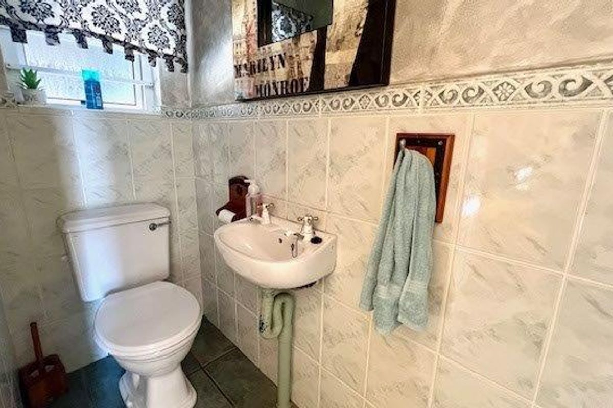 A compact bathroom featuring tiled walls and flooring, a standard toilet, and a wall-mounted basin.