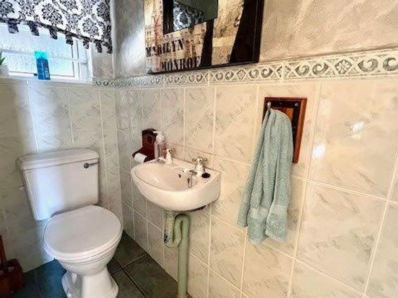 A compact bathroom featuring tiled walls and flooring, a standard toilet, and a wall-mounted basin.