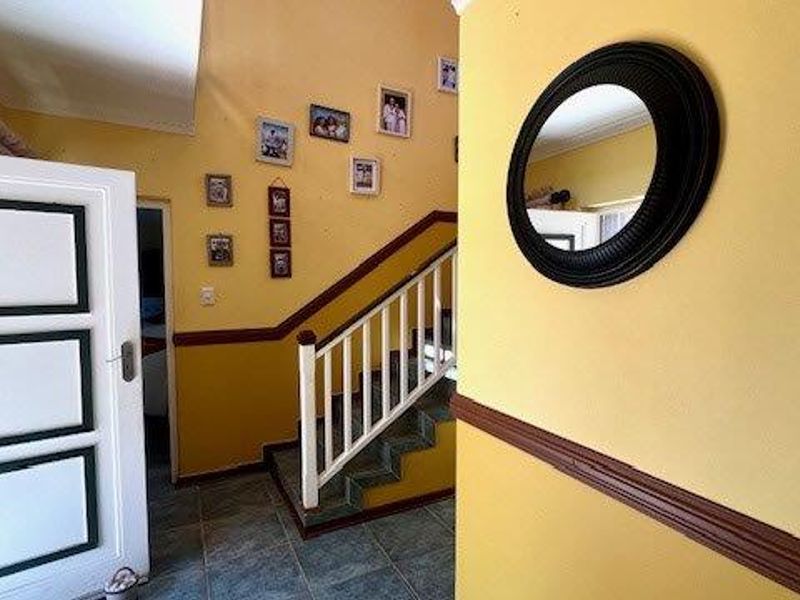 A bright hallway featuring a staircase with a wooden balustrade, tiled flooring, and decorative chair rail molding.