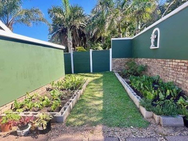 A well-maintained garden area featuring raised vegetable beds with concrete block edging, a central lawn path, and solid brick boundary walls.
