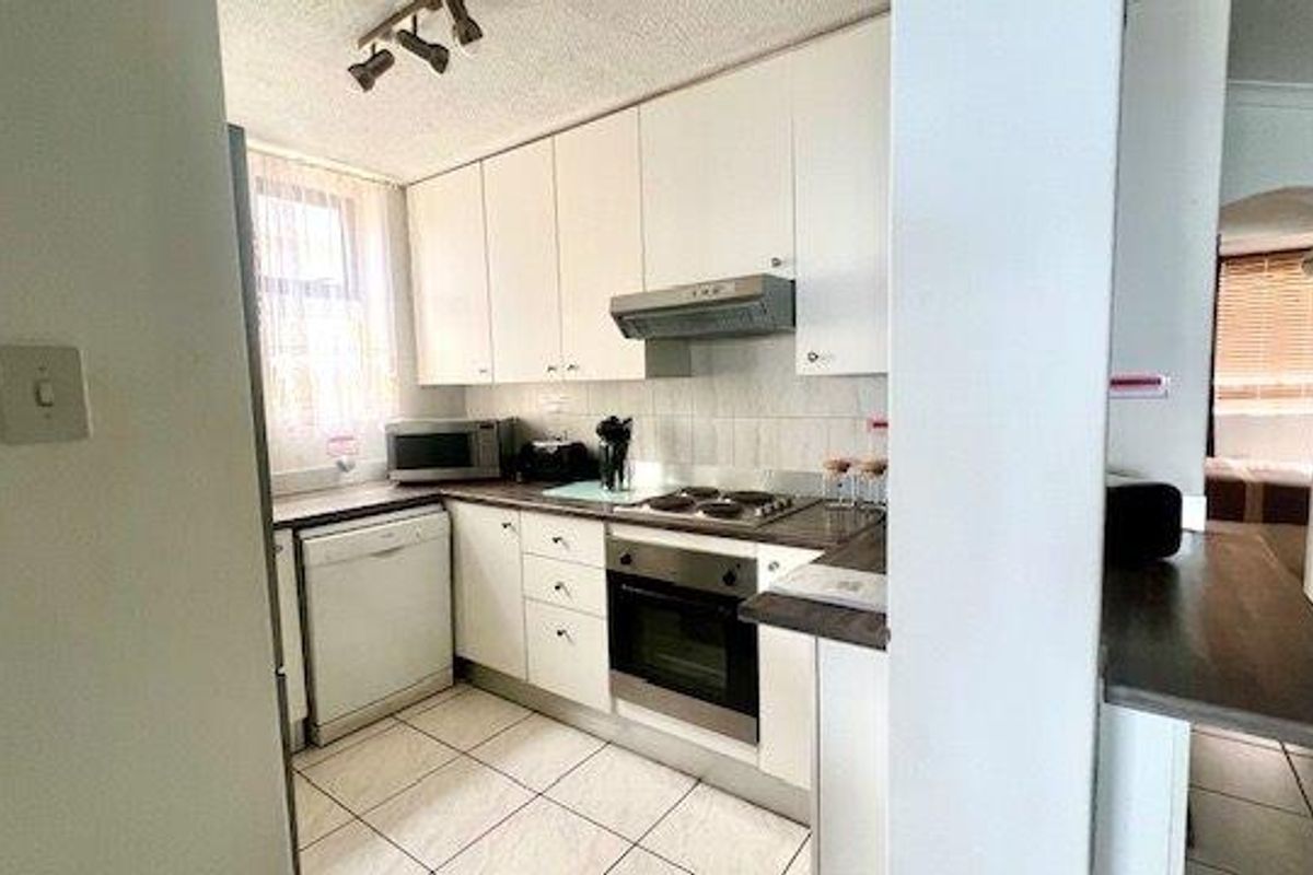 A functional kitchen featuring white cabinetry, dark laminate countertops, tiled backsplash, and integrated appliances including an oven and hob.