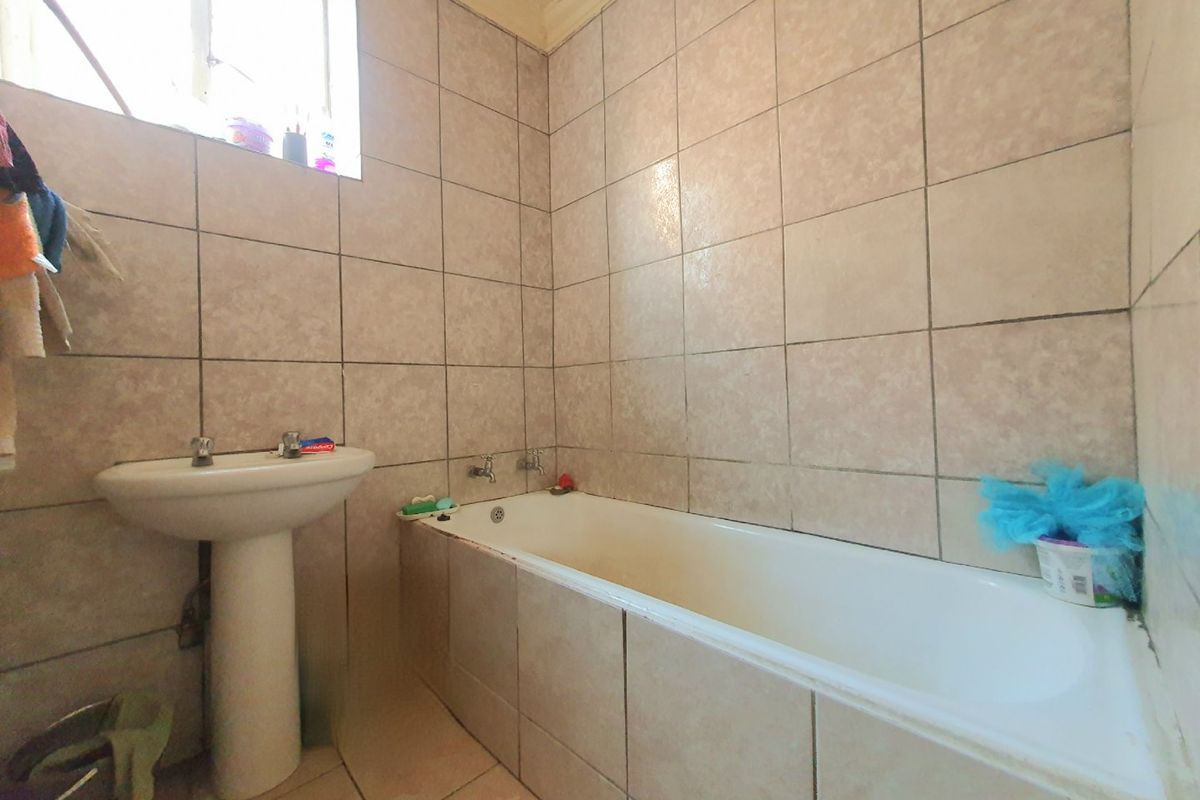 A functional bathroom featuring a pedestal basin and a built-in bathtub with full-height ceramic wall tiling.