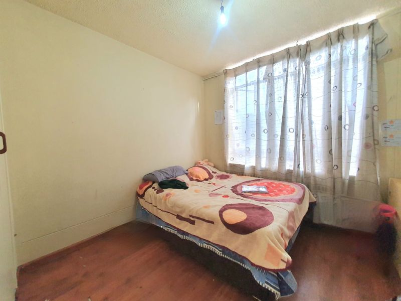 A bedroom featuring laminate flooring and a textured ceiling, currently requiring cosmetic updates to improve its overall condition and appeal.