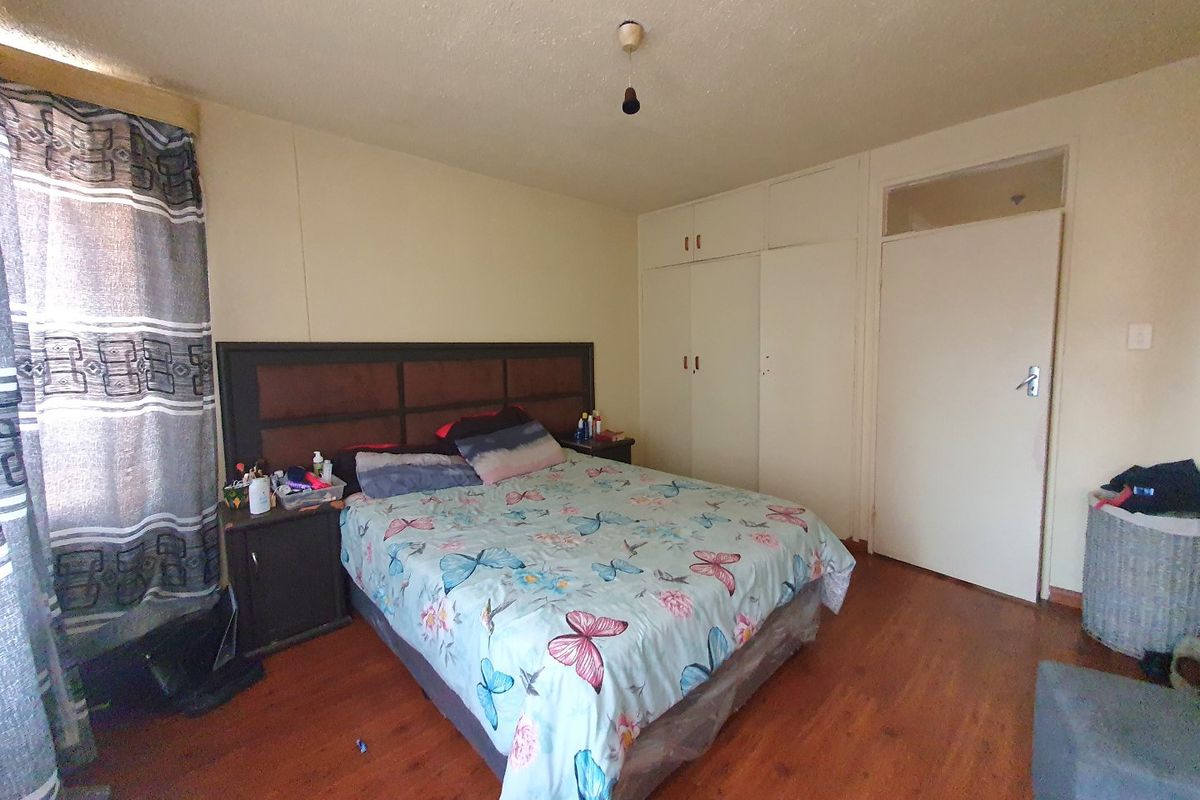 A bedroom featuring laminate flooring, built-in cupboards, and a transom window above the door. The room requires cosmetic updates to the ceiling and walls.