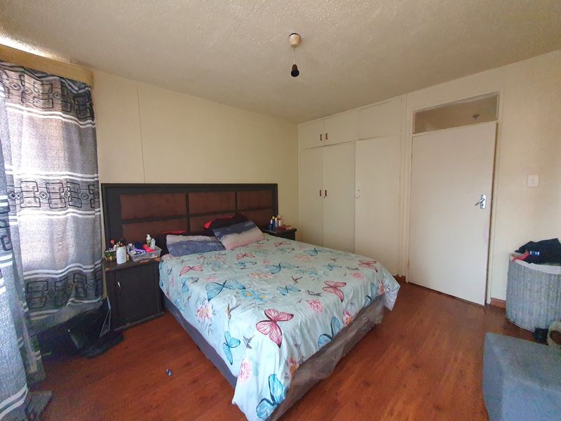 A bedroom featuring laminate flooring, built-in cupboards, and a transom window above the door. The room requires cosmetic updates to the ceiling and walls.