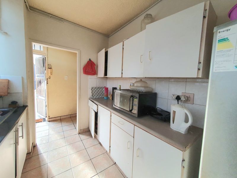 A functional kitchen featuring white built-in cabinetry, tiled flooring, and a tiled backsplash, offering a practical layout with direct access to the entrance area.