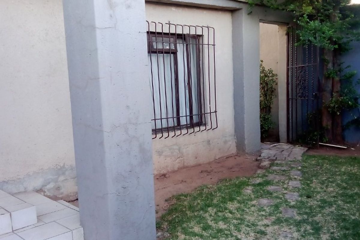 Rear exterior view of the property featuring concrete pillars, tiled steps, security bars on windows, and a small garden area with a security gate.