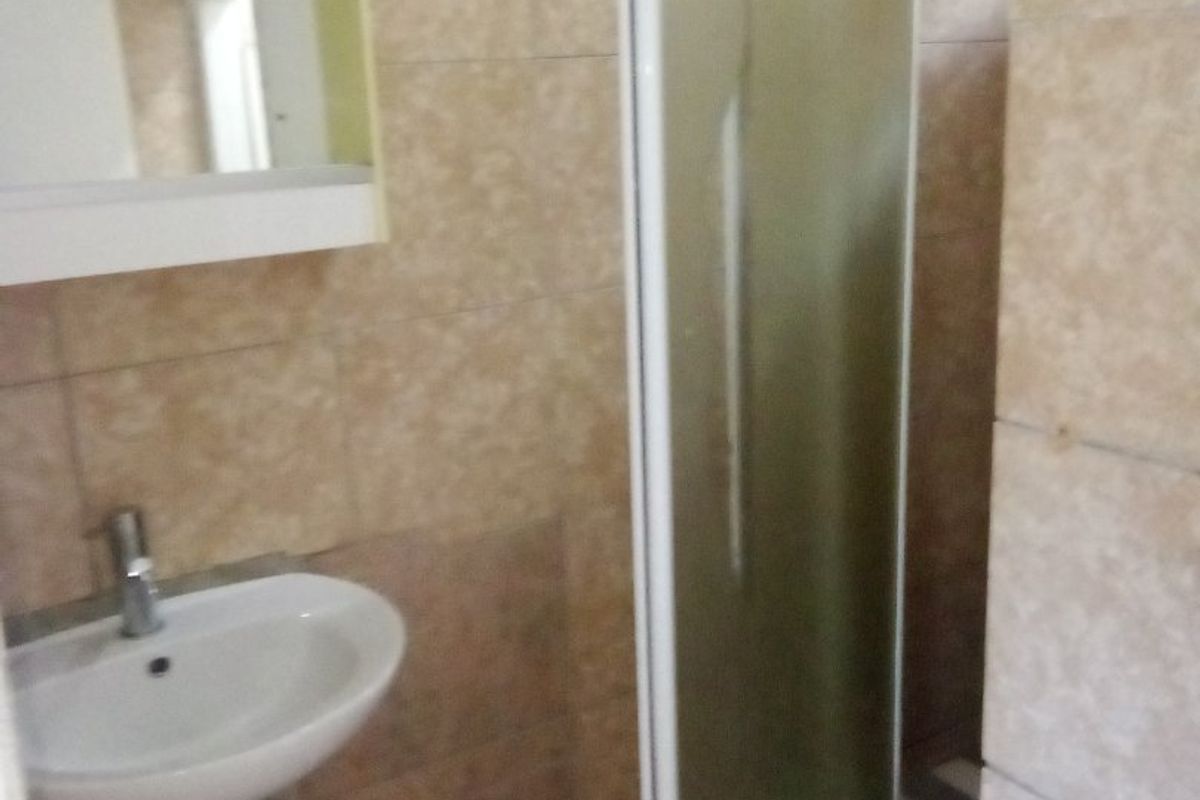 A functional bathroom featuring a pedestal basin, shower enclosure, and neutral wall tiling throughout.