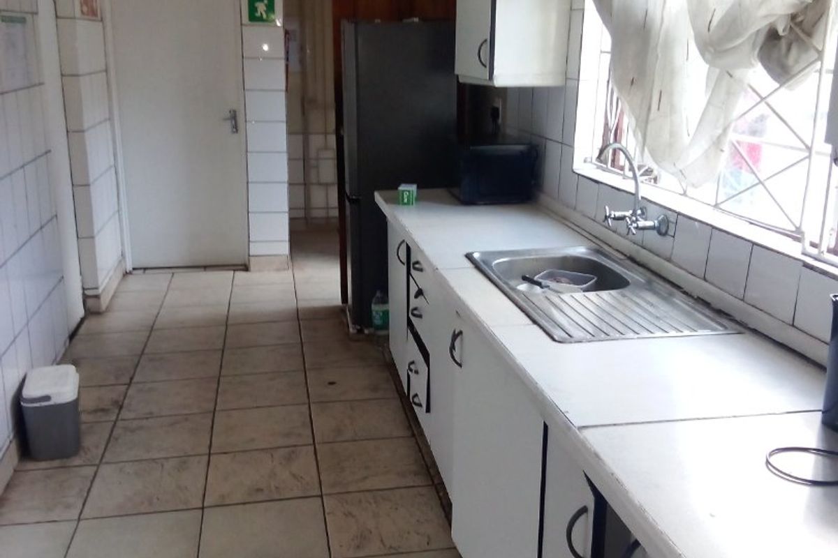 A functional kitchen featuring tiled walls and flooring, built-in cabinetry, and a stainless steel sink, offering potential for modernization and cosmetic updates.