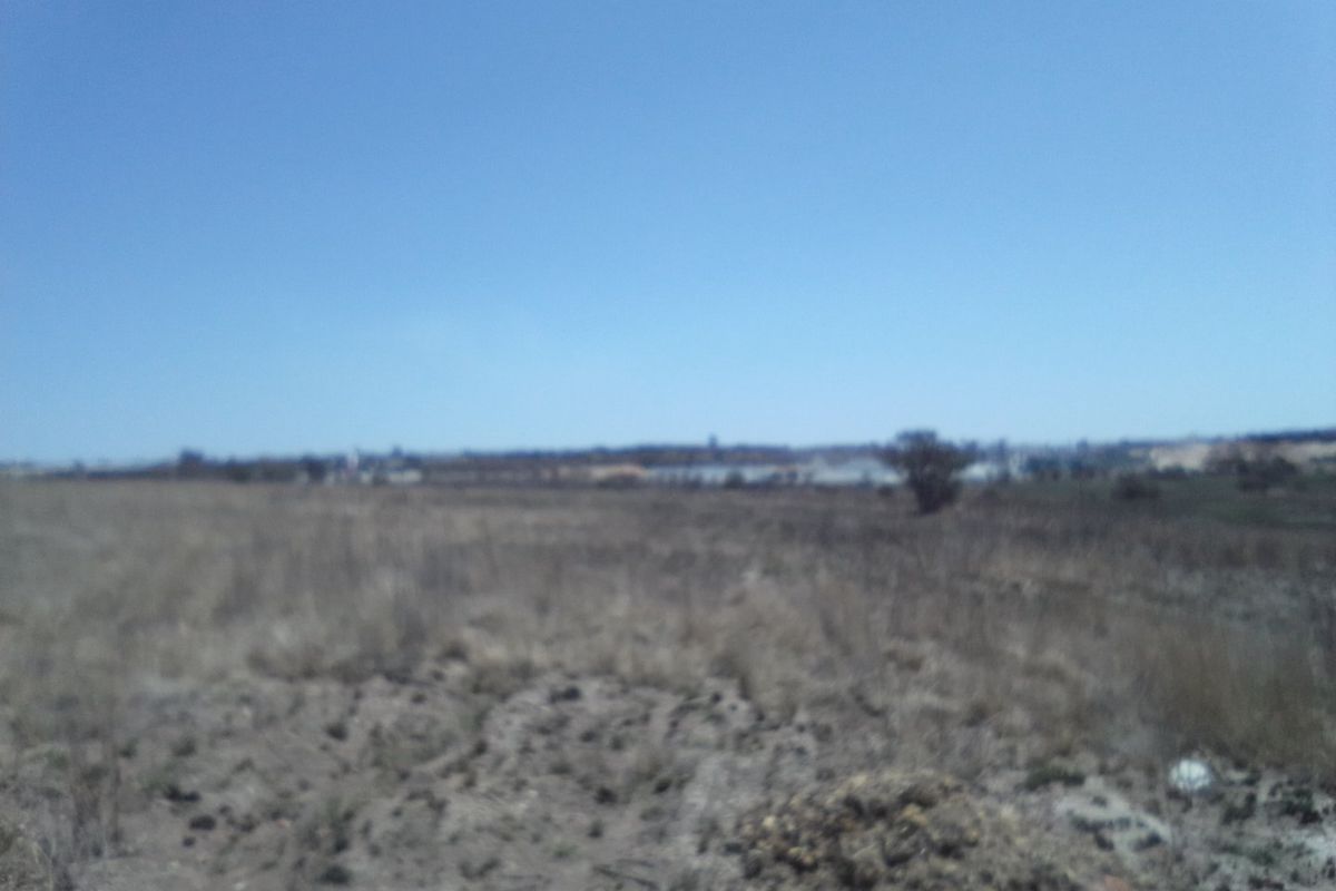 A wide-angle view of an undeveloped residential plot of land with natural vegetation under a clear blue sky.