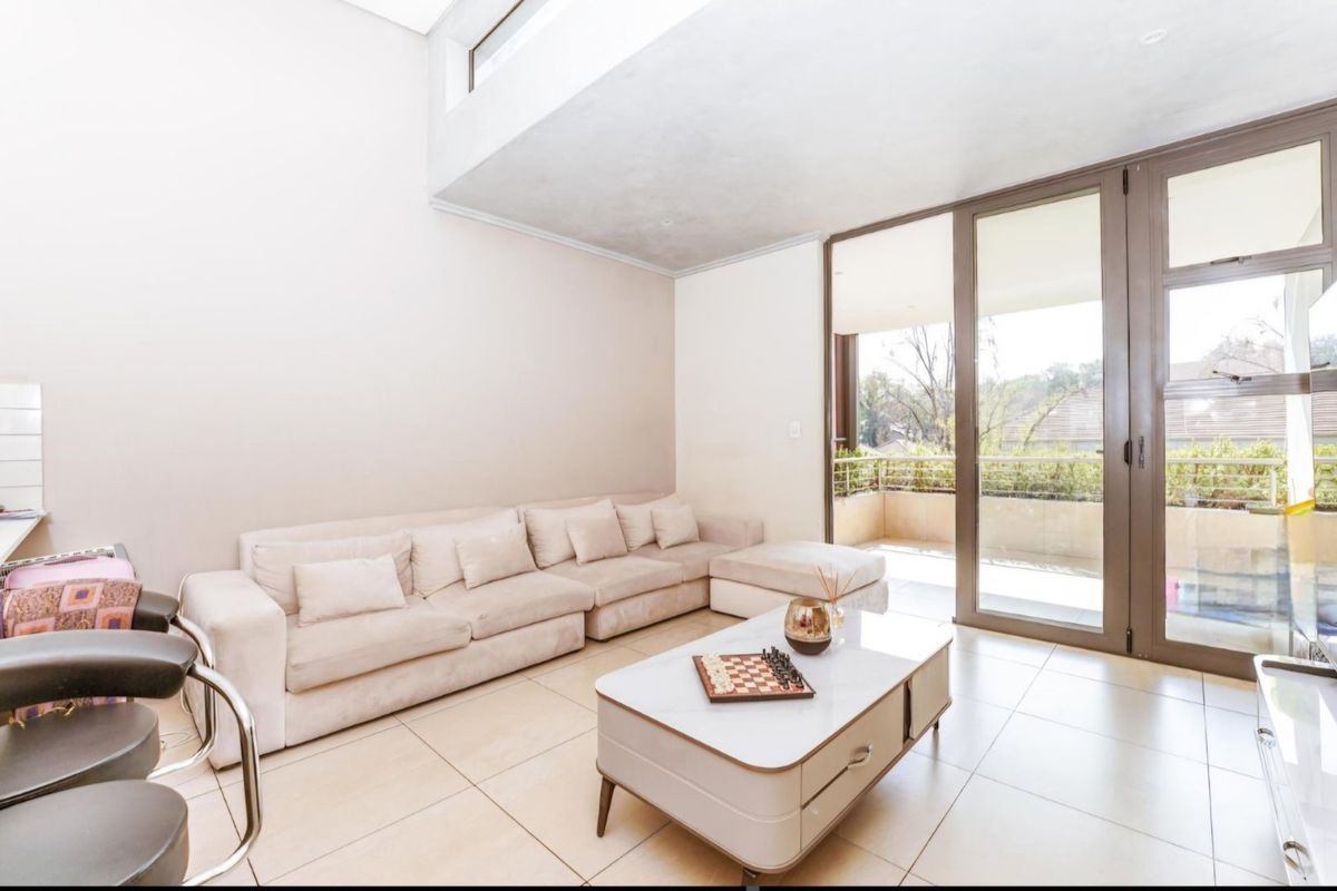 Bright and spacious living area featuring high ceilings, large format floor tiles, and seamless access to a private balcony through sliding glass doors.