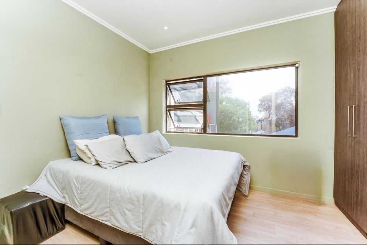 A well-maintained bedroom featuring light green walls, laminate flooring, a built-in wardrobe, and a large top-hung window providing natural light.
