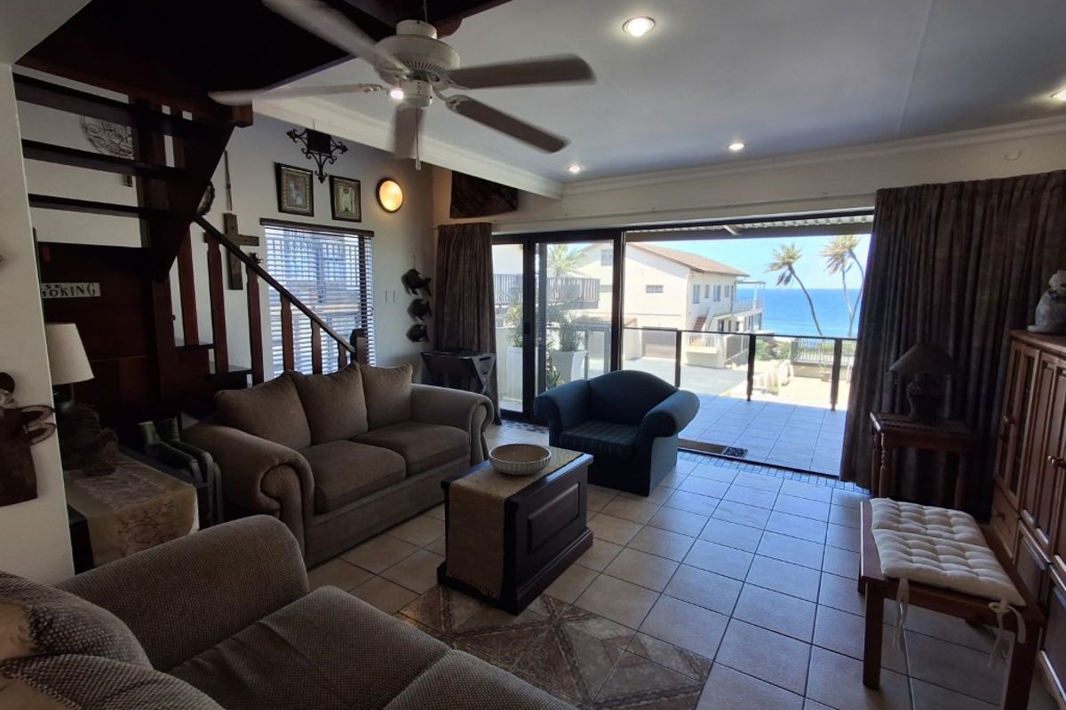 Spacious living room featuring tiled flooring, a ceiling fan, and large sliding glass doors that open onto a balcony with ocean views.