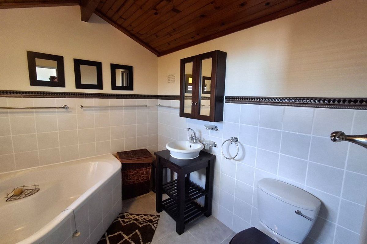 A bathroom featuring a built-in bathtub, vessel sink with vanity, toilet, and a timber-clad ceiling with tiled wall finishes.