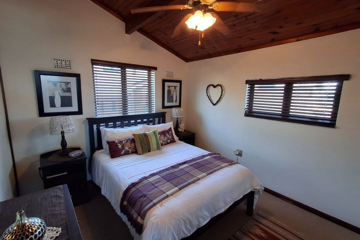 A cozy bedroom featuring a vaulted timber ceiling with an integrated ceiling fan and dual windows fitted with venetian blinds.