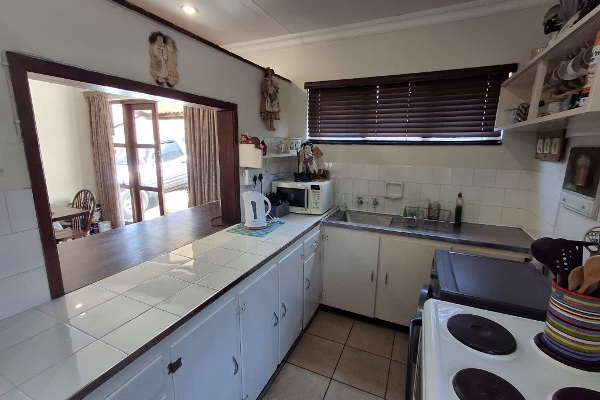 A functional kitchen featuring tiled countertops, built-in cabinetry, a stainless steel sink, and a convenient pass-through window overlooking the adjacent living area.
