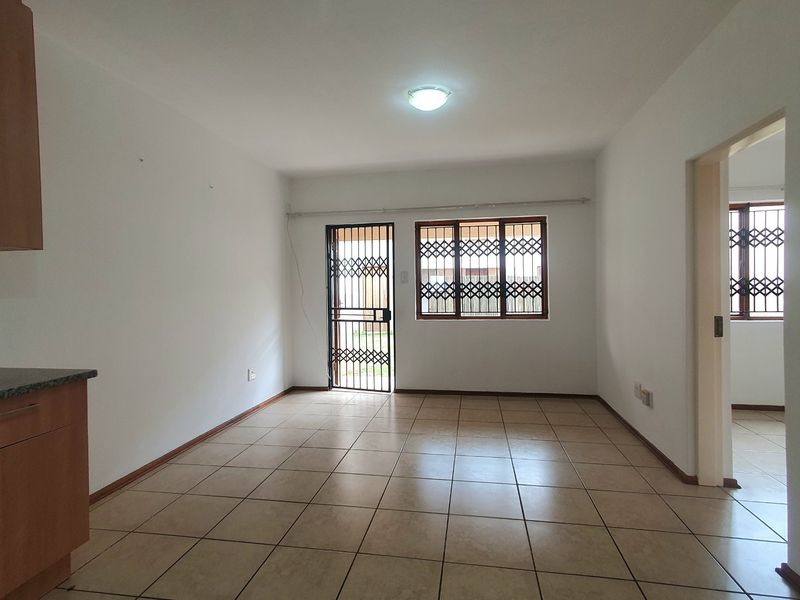 An empty open-plan living area featuring ceramic floor tiles, security gates, and window bars, offering a clean, neutral space ready for personalization.