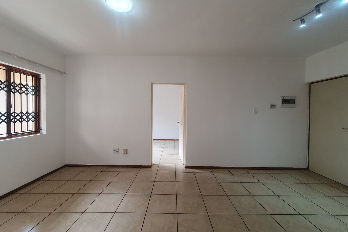 An empty, neutrally painted living area featuring tiled flooring, a security-gated window, and integrated electrical distribution board.