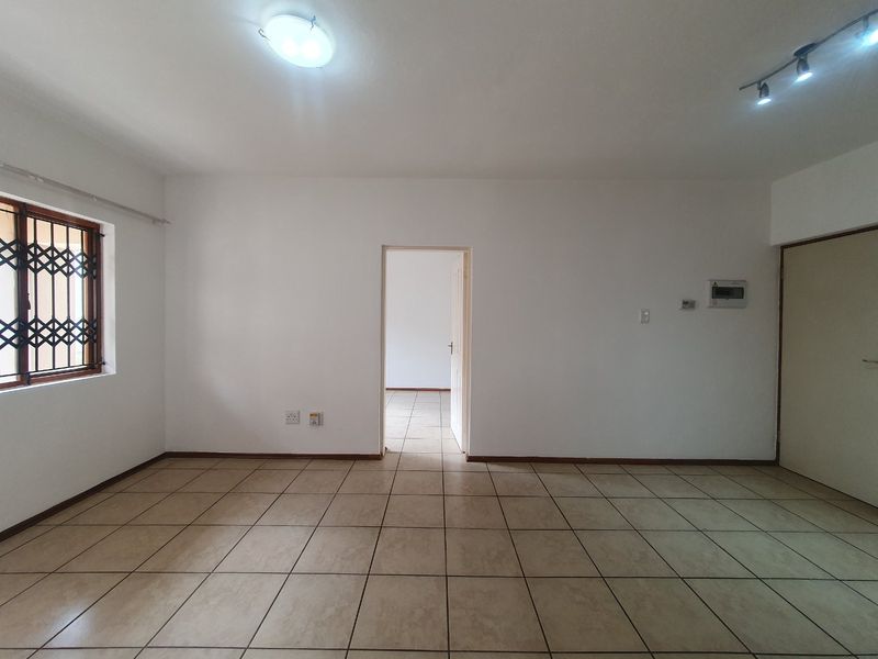 An empty, neutrally painted living area featuring tiled flooring, a security-gated window, and integrated electrical distribution board.