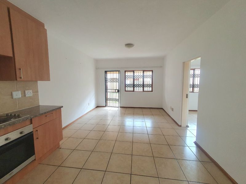 Open-plan living area featuring tiled flooring and a functional kitchen with built-in cabinetry, oven, and hob, leading to a secure exterior entrance.