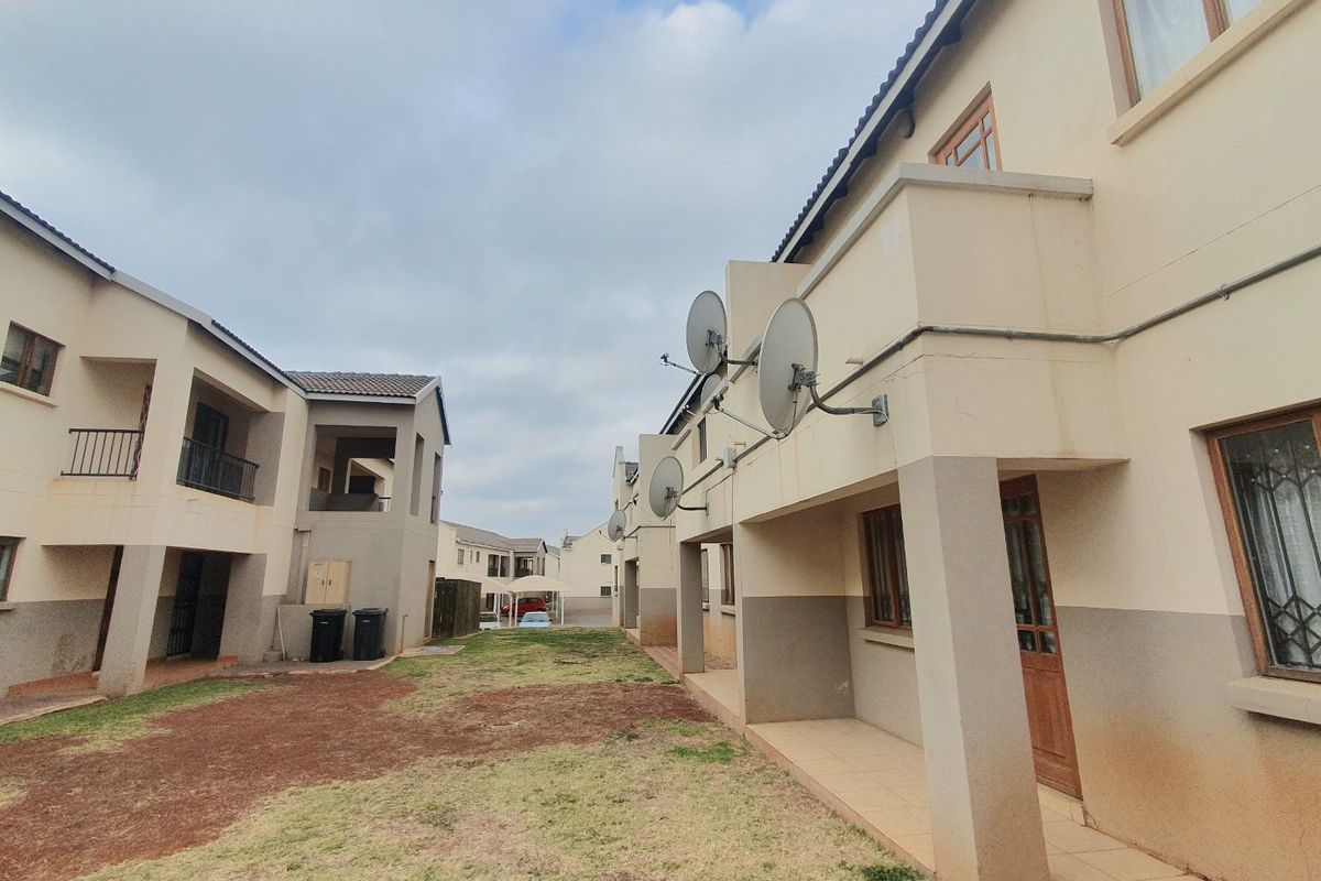 Rear view of townhouse complex showing shared garden space, tiled patios, and exterior building facades with mounted satellite dishes.