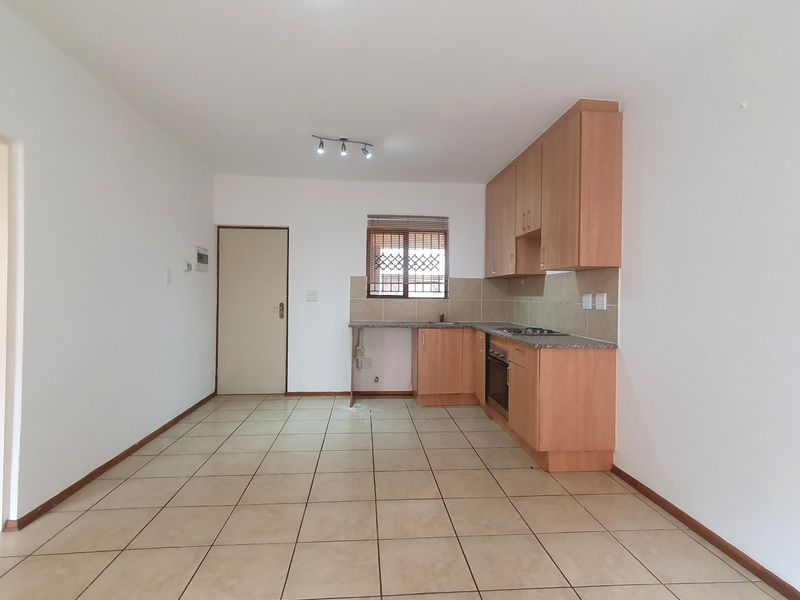 An open-plan kitchen area featuring light wood-finish cabinetry, laminate countertops, built-in oven and hob, and neutral tiled flooring throughout.