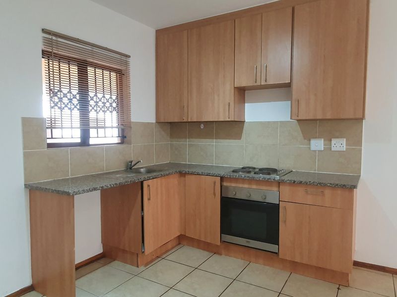 A functional kitchen featuring laminate cabinetry, granite countertops, a built-in oven, electric hob, and tiled backsplash with neutral floor tiles.