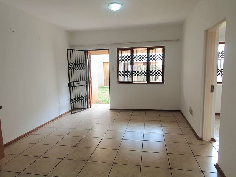 An empty living room featuring tiled flooring, security gates, and burglar bars, with direct access to an outdoor area.