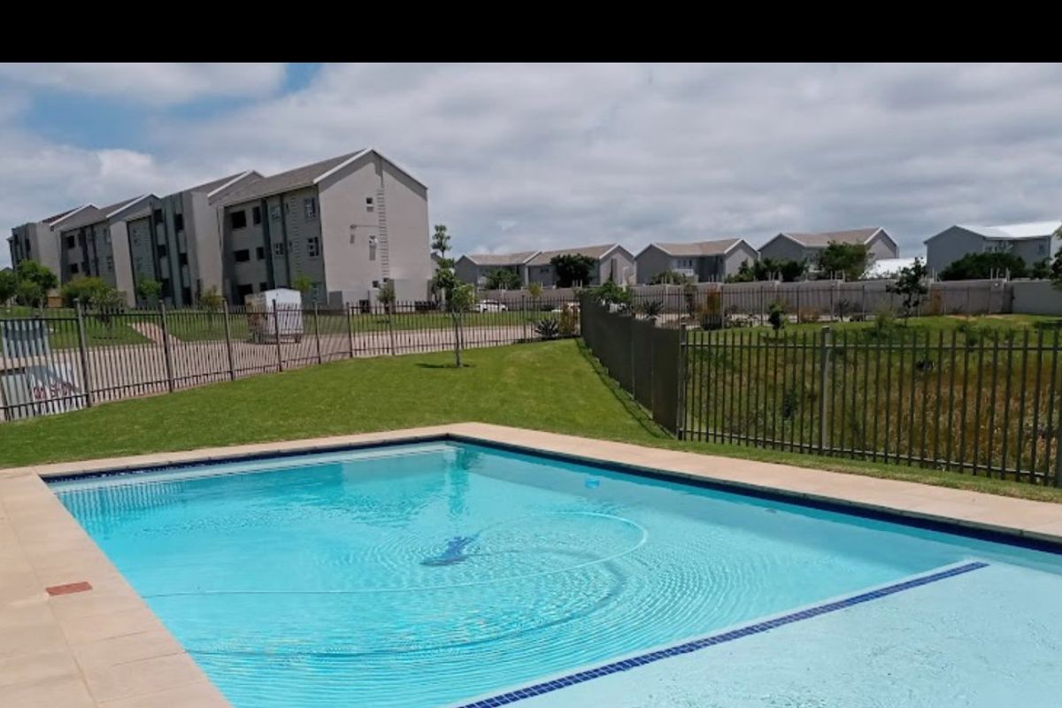 A communal swimming pool area featuring a paved surround and perimeter fencing, set within a residential apartment complex.