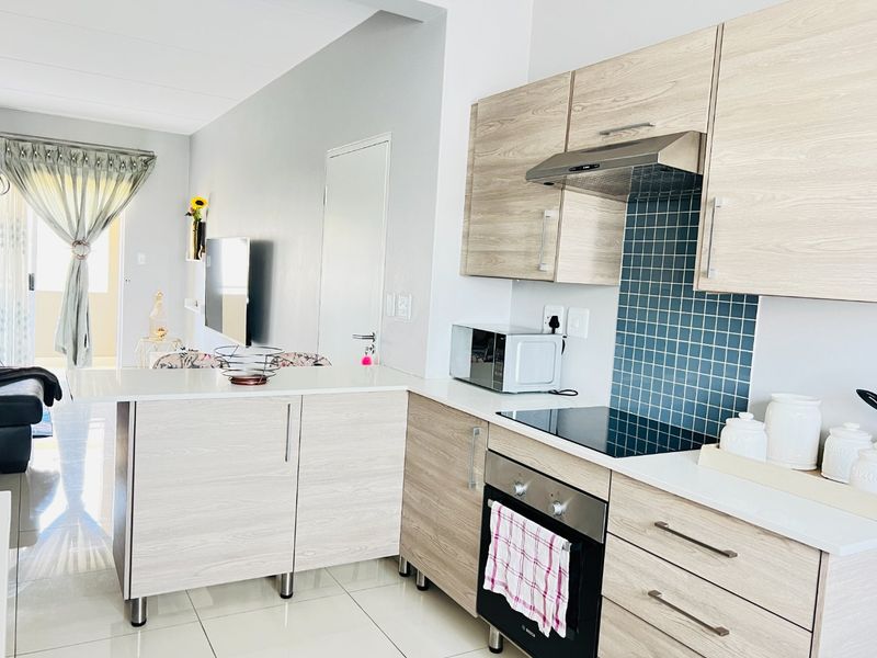 Modern open-plan kitchen featuring light wood-grain cabinetry, stone countertops, a sleek electric hob, and a tiled backsplash, seamlessly flowing into the living area.