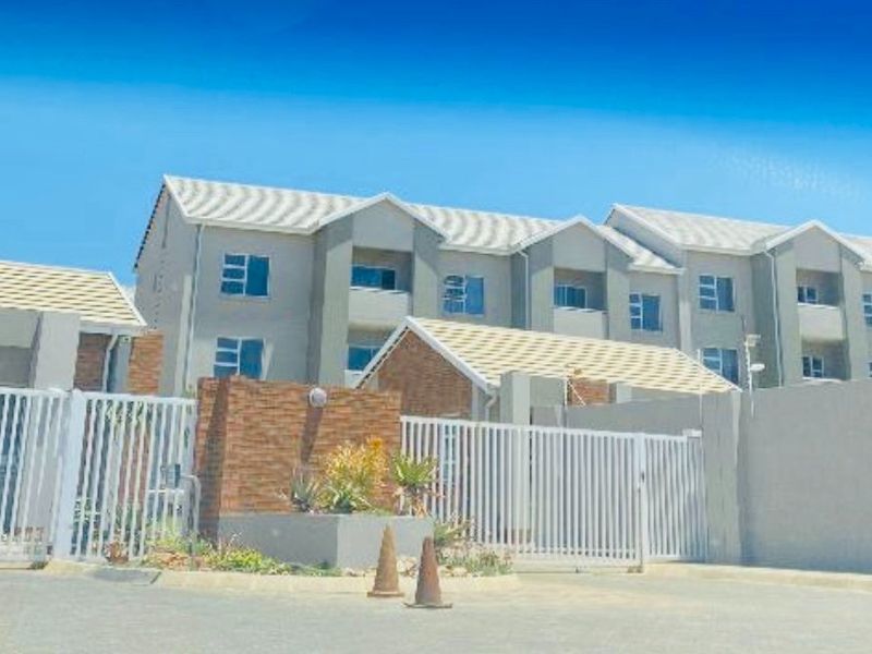 Front view of a modern apartment complex featuring a secure gated entrance, brick accents, and a paved driveway.