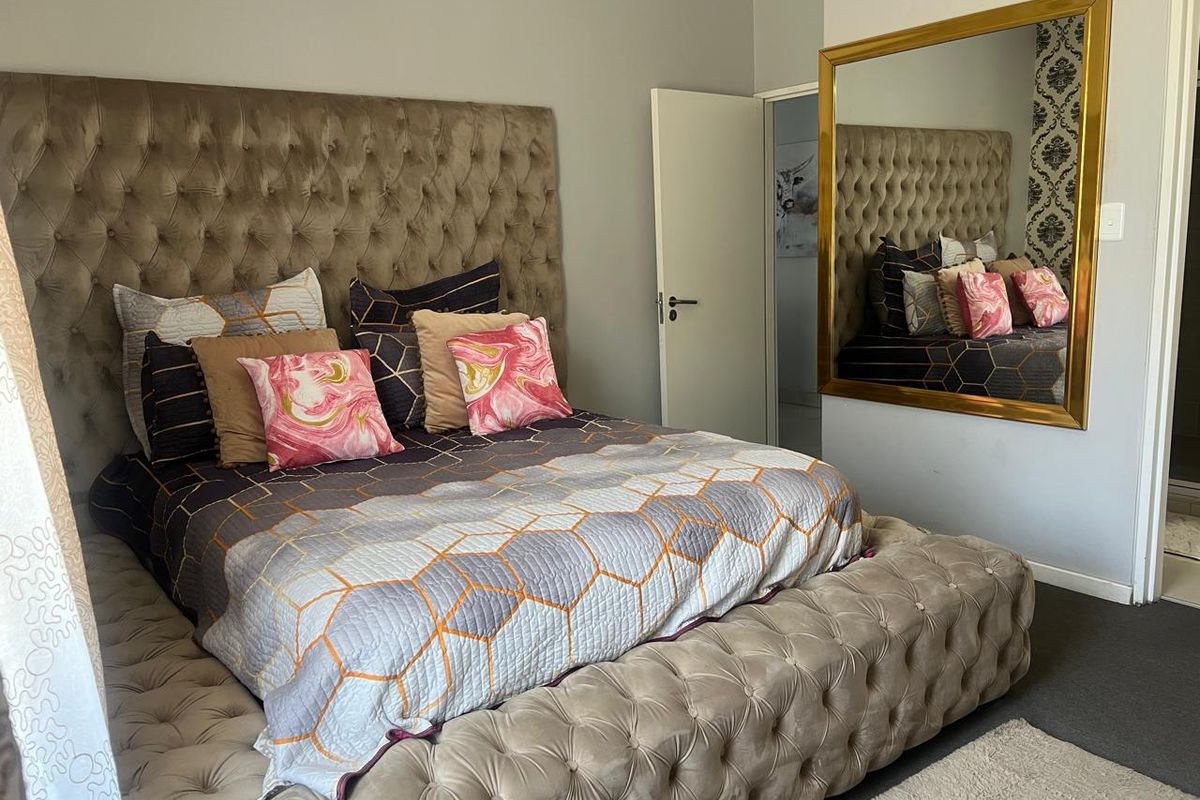 A well-maintained bedroom featuring neutral wall tones, a large wall-mounted mirror, and a standard interior door.