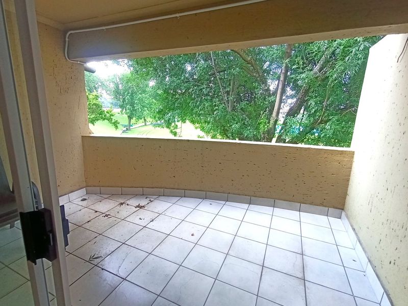 A covered balcony featuring tiled flooring and a concrete balustrade, offering a view of surrounding greenery.