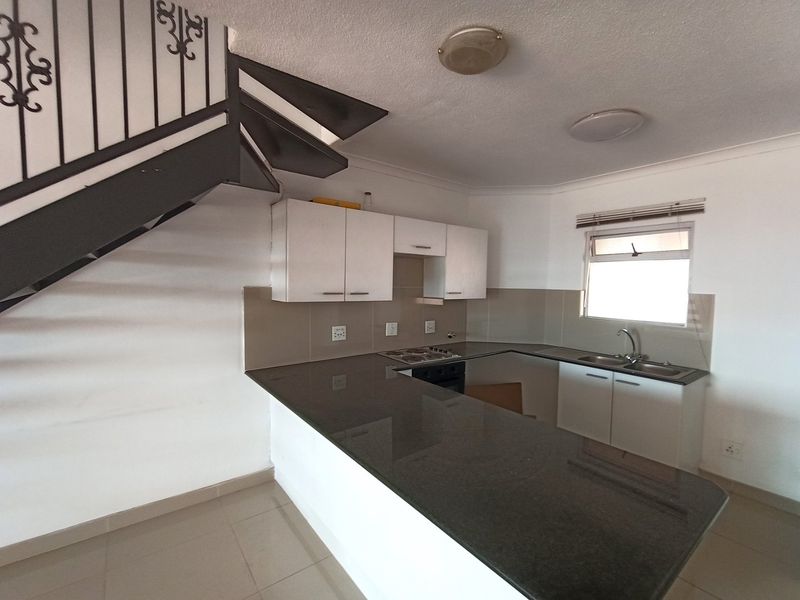 A functional kitchen featuring granite countertops, built-in cabinetry, and a built-in hob and oven, situated beneath an open-plan staircase.