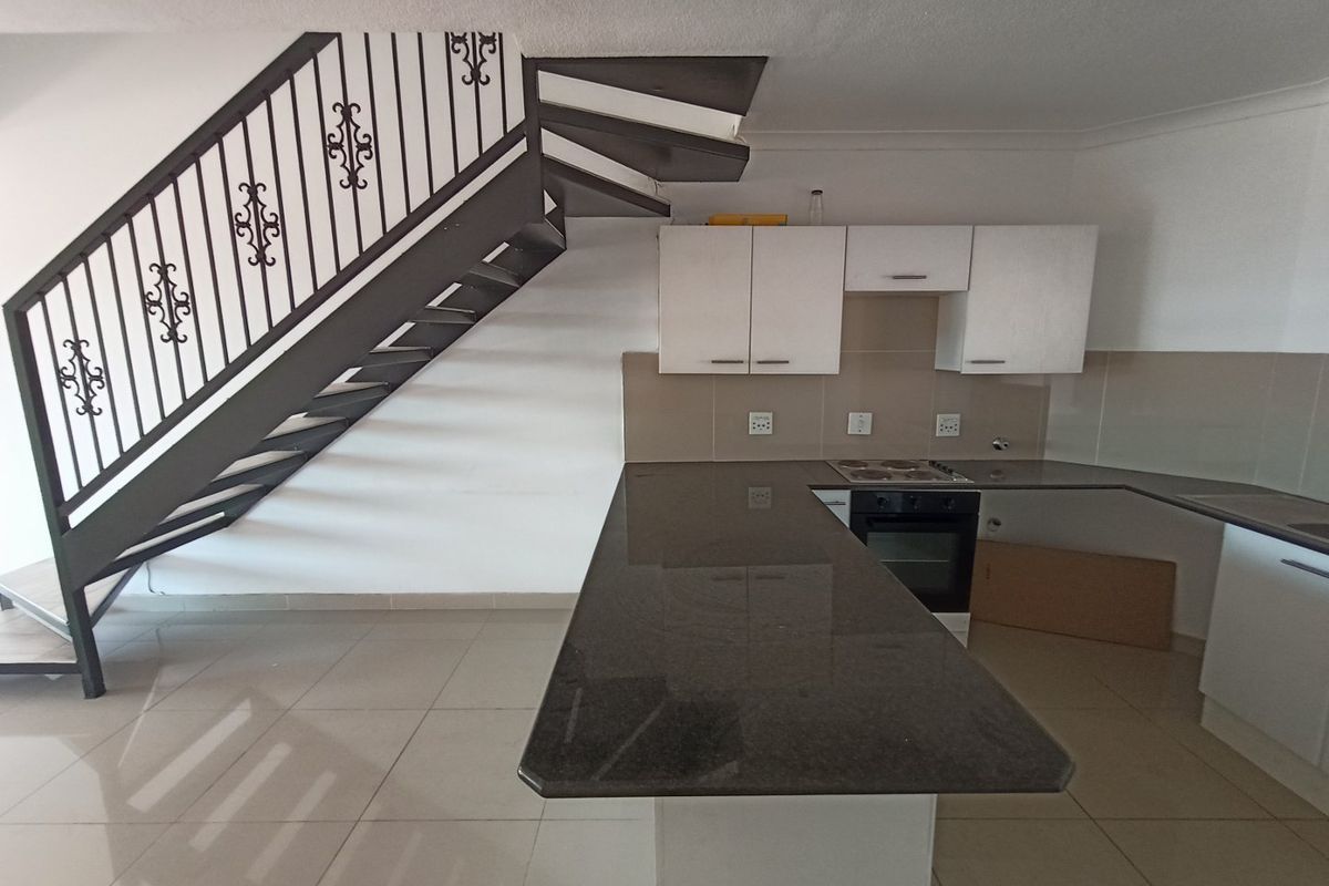 Open-plan kitchen featuring granite countertops, built-in oven, electric hob, and tiled flooring, situated adjacent to a wrought iron staircase.