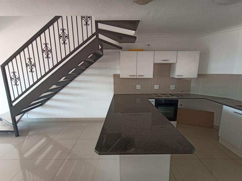 Open-plan kitchen featuring granite countertops, built-in oven, electric hob, and tiled flooring, situated adjacent to a wrought iron staircase.