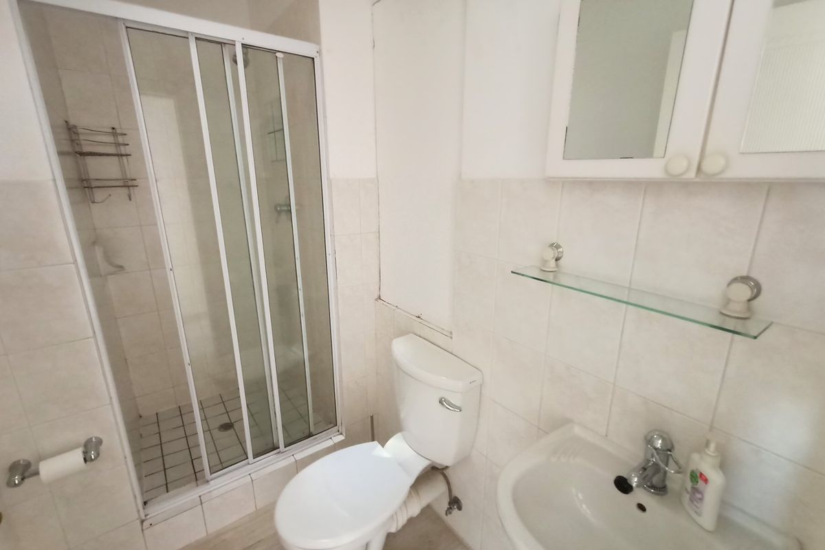 A functional bathroom featuring a shower enclosure, toilet, and wall-mounted basin with a medicine cabinet, finished with neutral wall and floor tiles.
