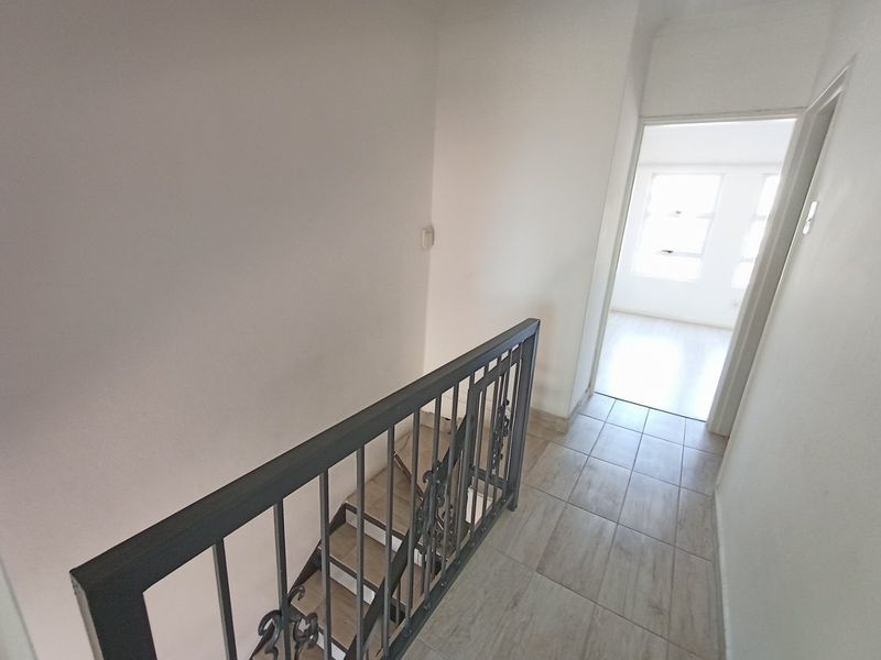 A bright hallway featuring tiled flooring and a wrought iron balustrade overlooking the staircase, leading into an adjacent room.