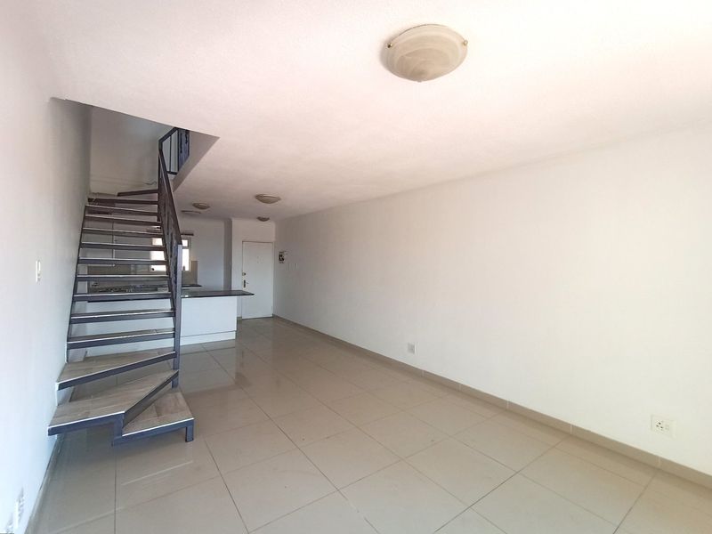 An open-plan living area featuring tiled flooring, a spiral staircase, and a kitchen breakfast bar, offering a clean and versatile space.