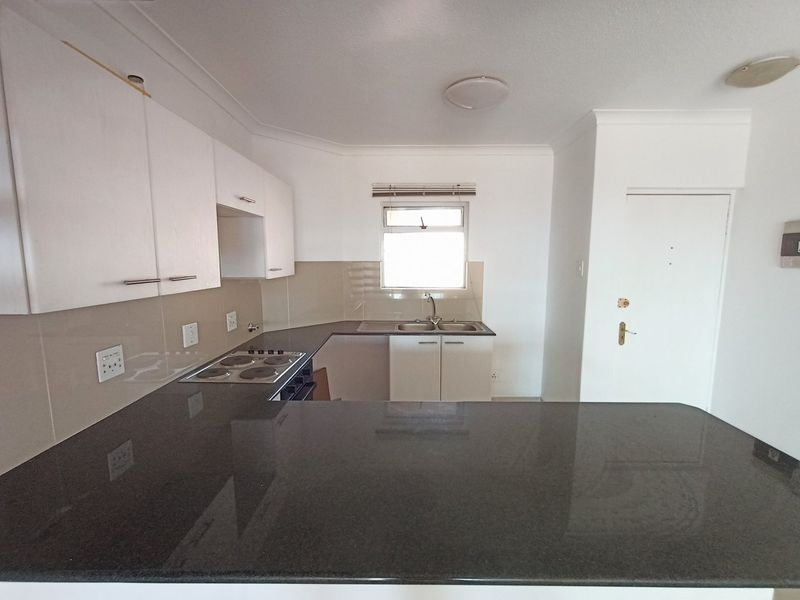 A functional kitchen featuring dark granite countertops, white cabinetry, an electric hob, and a double sink, presenting a clean and ready-to-use space.