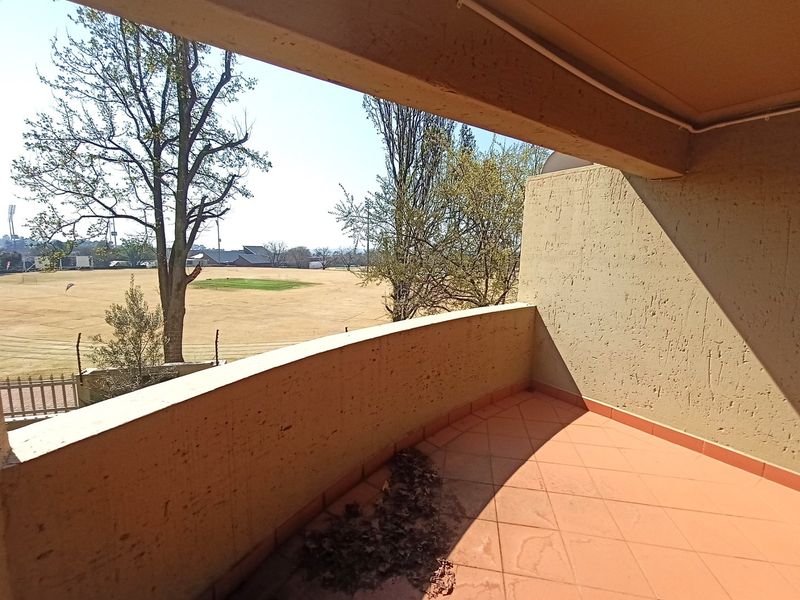 A covered balcony featuring tiled flooring and a concrete balustrade, offering an open view of the adjacent sports field.