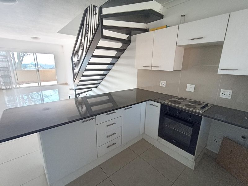 Modern open-plan kitchen featuring sleek white cabinetry, granite countertops, and integrated appliances, seamlessly flowing into the living area with staircase access.