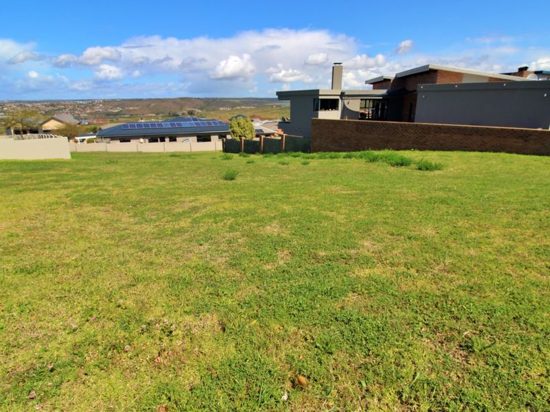 A vacant residential plot featuring a level grass lawn with established boundary walls and surrounding neighborhood views.