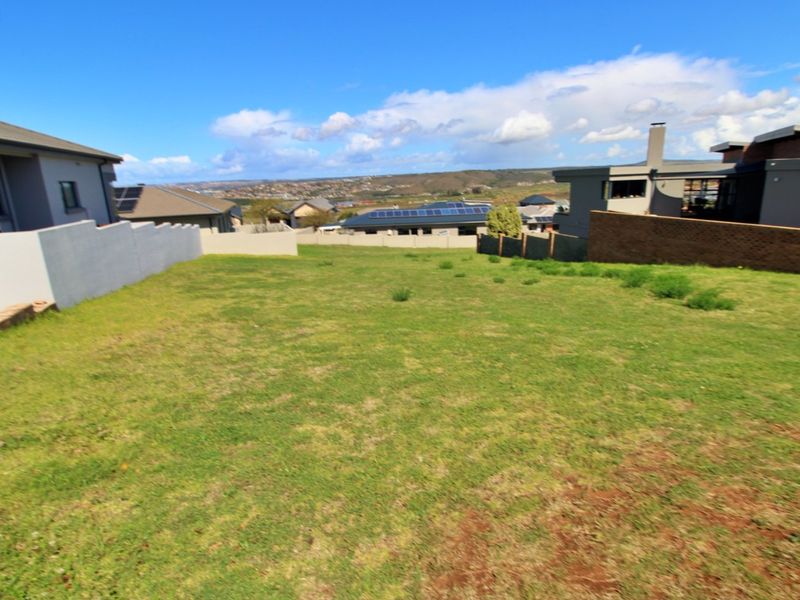 A vacant residential plot featuring a grassed area, enclosed by boundary walls and fencing, situated within a developed neighborhood.