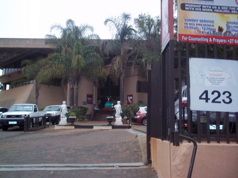 Front exterior view of a commercial property featuring a paved driveway, concrete facade, and security fencing with prominent signage.