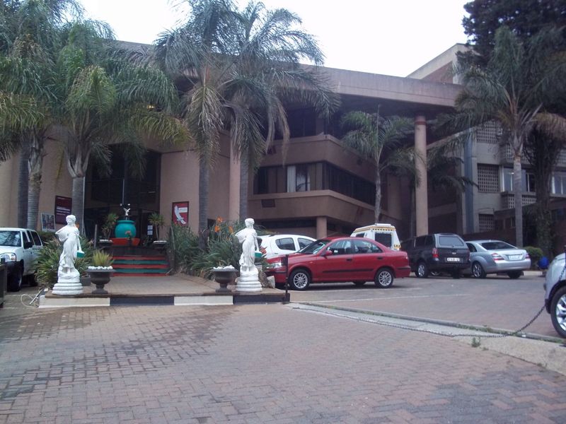Front exterior view of a multi-story commercial building featuring a paved driveway, concrete structural columns, and established palm tree landscaping.