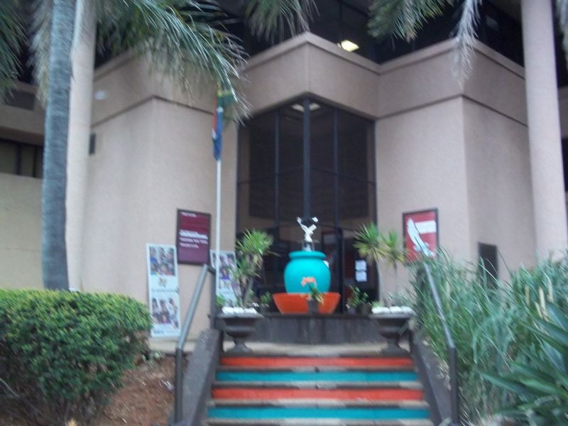 Front entrance of a commercial building featuring a concrete staircase with metal handrails, a glass facade, and a central decorative fountain.