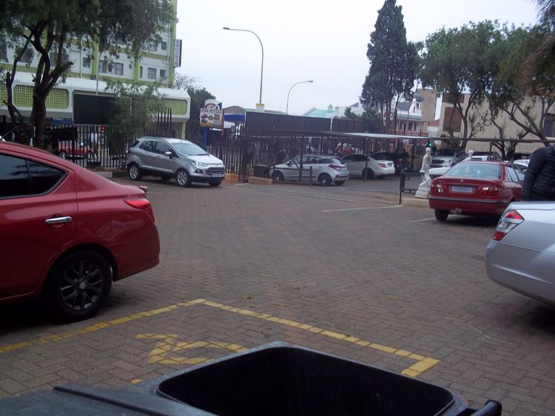 An outdoor paved parking area featuring marked bays and a covered carport structure, situated within a commercial property setting.