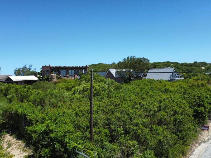 A vacant residential plot covered in dense coastal vegetation, situated in a developed neighborhood with established homes nearby.